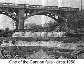 Black and white photo of two tiers of low waterfalls, in front of a bridge--one of the Cannon falls, circa 1950