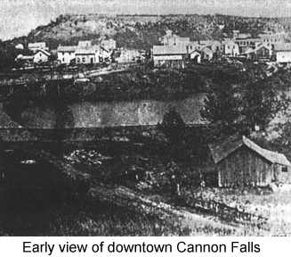 Black and white photo showing houses and stores on a low bluff across a river--early view of downtown Cannon Falls