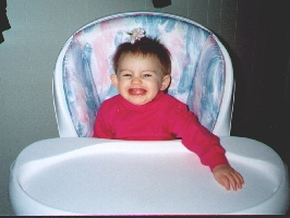 Picture of Emily sitting at a high chair and grinning exhuberantly