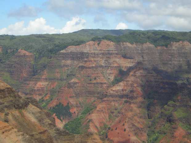 Straight ahead a massive wall rises up in thin horizontal layers of pink, red, and grey, surmounted by thick forest with low mountains beyond. Straight ahead a massive wall rises up in thin horizontal layers of pink, red, and grey, surmounted by thick forest with low mountains beyond.