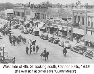 Black and white  photograph of the west side of 4th. St. Cannon Falls, looking north, in the 1930s; an oval sign over a one-story shop about halfway up the street says 'Quality Meats'