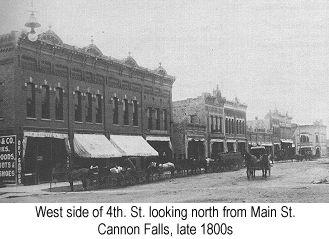 IMAGE/PHOTO: West side of 4th. St., looking north from Main St. Cannon Falls, late 1890s: Black and white photo showing several brick-fronted Italianate two-story store buildings with broad fabric awnings over the sidwalk at the left, followed to the right by a single-story building with awning folded back, two two-story buildings with folded-back awnings, a long one-story building, a two-story building at the corner, and another two-story building on the other side of the corner in the distance. Horses and wagons are parked in front of the buildings and a carriage drawn by two horses is coming down the dirt street towards the camera.